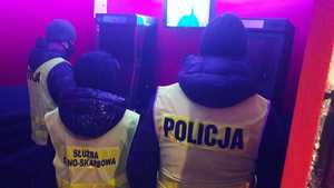 na zdjęciu dwaj policjanci i funkcjonariusz Urzędu Cywilno skarbowego przy automatach do gier.